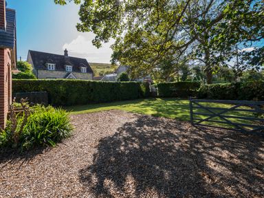 A garden with gravel driveway and green lawn with trees and a house in the background at St Marys Chapel in West Lulworth
