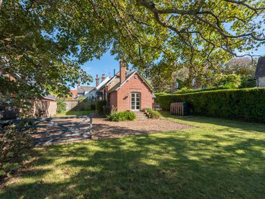 A brick house with a gravel driveway and a wooden gate surrounded by grass and trees at St Mary's Chapel in West Lulworth