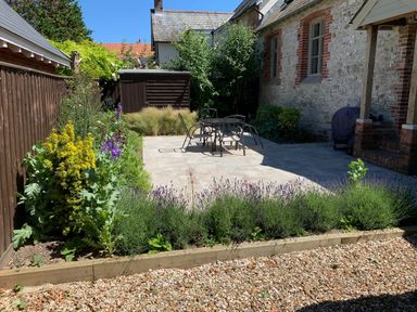 A garden with a patio area and metal table and chairs surrounded by plants and a gravel pathway at St Mary's Chapel in West Lulworth