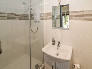 A bathroom with a shower enclosure a white sink with cabinet a mirror and a soap dispenser at The Garden House in Upper Quinton near Lower Quinton