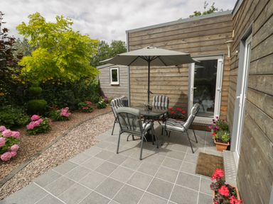 An outdoor patio with a table and four chairs under an umbrella surrounded by plants and flowers at The Garden House in Upper Quinton near Lower Quinton