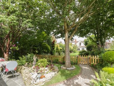 A garden with trees shrubs a stone flower bed and a wooden fence at The Garden House in Upper Quinton near Lower Quinton