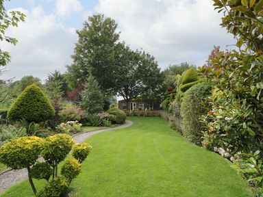 A garden with a green lawn surrounded by shaped bushes trees and flowers at The Garden House in Upper Quinton near Lower Quinton