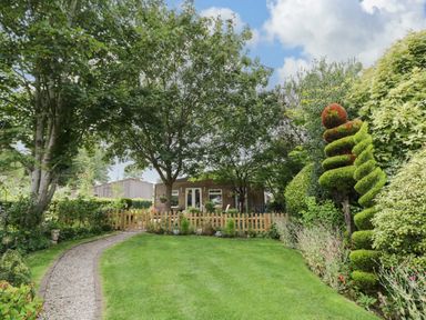 A garden with a gravel path leading to a wooden fence and a house surrounded by trees and bushes at The Garden House in Upper Quinton near Lower Quinton