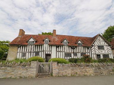 A timber-framed house with a tiled roof behind a stone wall and wooden gate at The Garden House in Upper Quinton near Lower Quinton