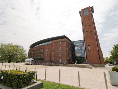 A large brick building with a tall tower and glass entrance with rsc signs outside