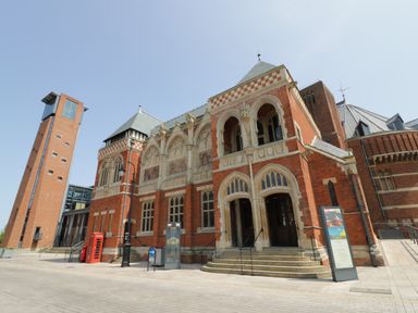 A historic brick building with arched entrances and a clock tower with a red telephone box outside