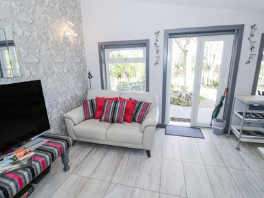 A sitting area with a white sofa with cushions a television and patio doors leading outside at The Garden House in Upper Quinton near Lower Quinton
