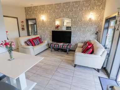 A living room with two white sofas with red and striped pillows a TV on a striped table and a white table with flowers at The Garden House in Upper Quinton near Lower Quinton