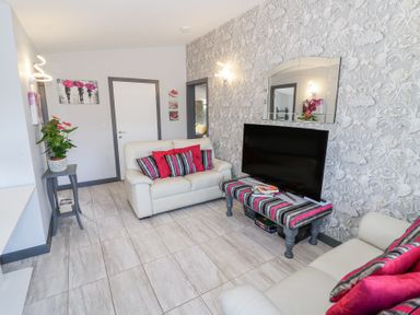 A living room with two white sofas and a striped table holding a television at The Garden House in Upper Quinton near Lower Quinton