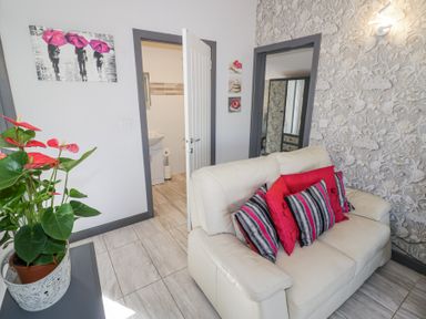 A living room with a white sofa and red and striped cushions a patterned wallpaper a plant in a pot and doors leading to other rooms at The Garden House in Upper Quinton near Lower Quinton
