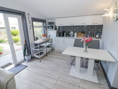 A kitchen with white cabinets a dining table with chairs and flowers and glass doors leading outside at The Garden House in Upper Quinton near Lower Quinton