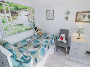A bedroom with a bed with patterned bedding stuffed bears a chair and a bedside table with a lamp at The Garden House in Upper Quinton near Lower Quinton