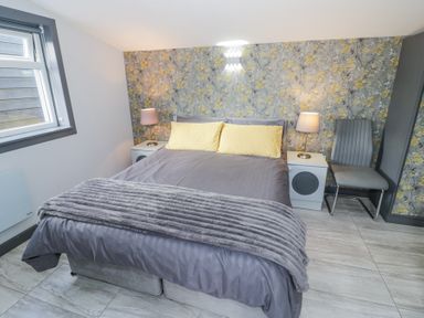 A bedroom with a double bed yellow pillows bedside tables with lamps patterned wallpaper and a chair at The Garden House in Upper Quinton near Lower Quinton