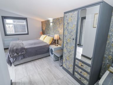 A bedroom with a bed yellow pillows bedside tables lamps a wardrobe with mirror and floral wallpaper at The Garden House in Upper Quinton near Lower Quinton