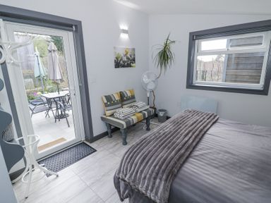 A bedroom with a bed a bench with folded towels a standing fan a coat rack and a door opening to a patio at The Garden House in Upper Quinton near Lower Quinton
