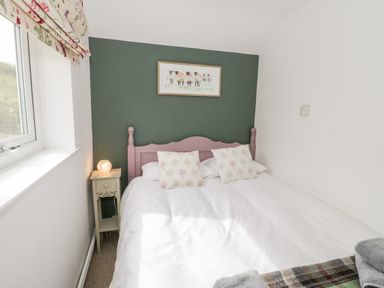 A bedroom with a double bed white bedding two patterned pillows green accent wall a bedside table with lamp and a window at Afallon in Penmachno