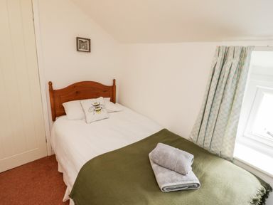 A bedroom with a wooden bed having white linens and a bee pillow with folded towels on an olive blanket at Afallon in Penmachno