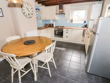 A kitchen with wooden table and white chairs tiled floor and blue tiled backsplash at Afallon in Penmachno