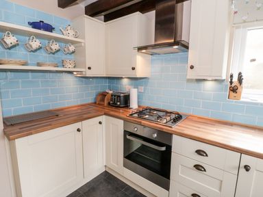 A kitchen with white cabinets wooden countertops blue tiled backsplash and kitchen appliances at Afallon in Penmachno