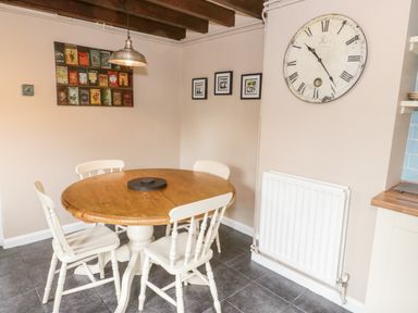 A dining area with a round wooden table and four white chairs a large wall clock and framed pictures on walls at Afallon in Penmachno