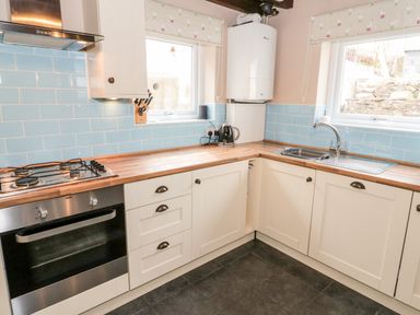 A kitchen with wooden countertops white cabinets blue tile backsplash and stainless steel oven at Afallon in Penmachno