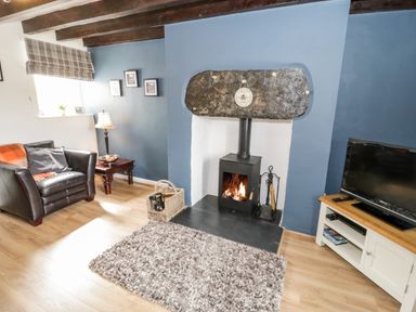 A living room with a wood stove fireplace a chair a side table and a television at Afallon in Penmachno