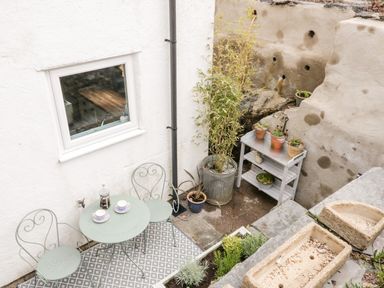 A small outdoor patio with a round metal table and two chairs a potted plant and small garden at Afallon in Penmachno