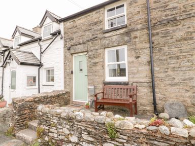 Stone cottage exterior with a light green door wooden bench and stone wall at Afallon in Penmachno