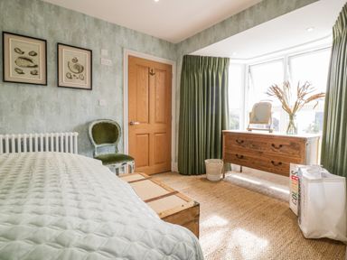 A bedroom with a wooden door green curtains a wooden dresser a green chair and framed pictures on the wall at Louvain Cadgwith near Ruan Minor
