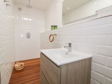 A bathroom with a wooden floor a sink with cabinet green bottles and a shower area at Louvain Cadgwith near Ruan Minor