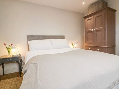 A bedroom with a bed a bedside table with a lamp and flowers and a wardrobe at Louvain Cadgwith near Ruan Minor