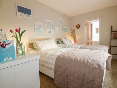 A bedroom with two single beds a bedside table with flowers and a book and framed pictures on the wall at Louvain in Cadgwith near Ruan Minor