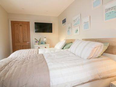 A bedroom with a double bed two pillows a nightstand with books and a radio and a wall mounted TV at Louvain in Cadgwith near Ruan Minor