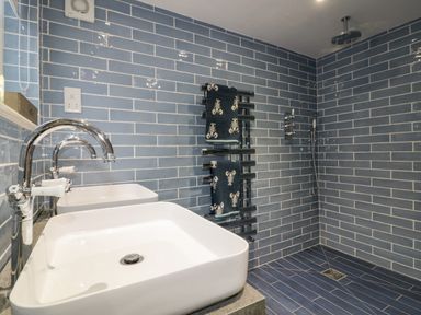 A bathroom with two white sinks a chrome faucet a heated towel rail with lobsters towel and a walk in shower at Louvain in Cadgwith near Ruan Minor