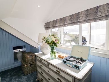 A room with a dresser holding a vase of flowers a lamp and a record player near a window at Louvain in Cadgwith near Ruan Minor