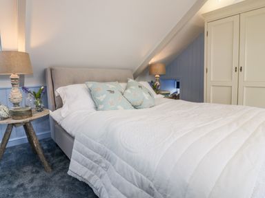 A bedroom with a bed with patterned pillows bedside tables with lamps and flowers and a wardrobe at Louvain in Cadgwith near Ruan Minor