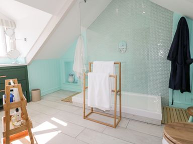 A bathroom with a walk-in shower a towel rack with white towels a black robe hanging on the wall and a green cabinet at Louvain Cadgwith near Ruan Minor