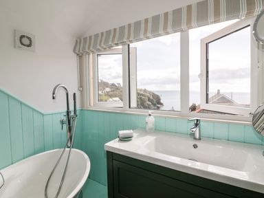 A bathroom with a bathtub shower faucet sink and windows overlooking a coastal view at Louvain in Cadgwith near Ruan Minor