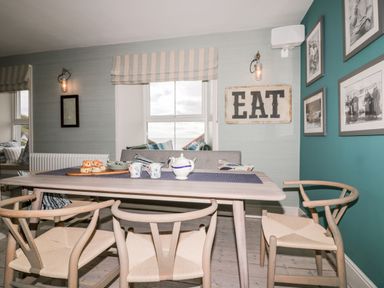 A dining area with a wooden table and chairs with a sign that says eat on the wall at Louvain in Cadgwith near Ruan Minor