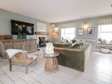 A living room with an olive green sofa a wicker side table and a large TV on a wooden cabinet at Louvain in Cadgwith near Ruan Minor