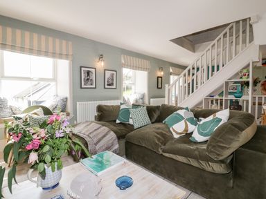 A living room with a green sofa and patterned cushions a bouquet of flowers on a wooden table under stairs at Louvain in Cadgwith near Ruan Minor