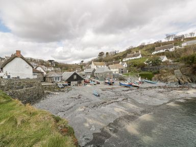 A small coastal village with boats on a beach and white cottages on a hillside at Louvain in Cadgwith near Ruan Minor