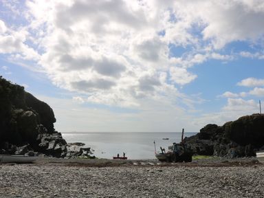 A rocky beach with boats and people near the water at Louvain in Cadgwith near Ruan Minor