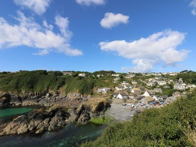 A coastal village with houses on a hillside by a rocky shore and clear water at Louvain in Cadgwith near Ruan Minor