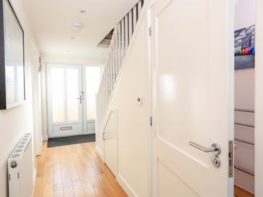 A hallway with wooden floor a radiator a front door stairs and a partially open door at 2 The Bay in Bigbury