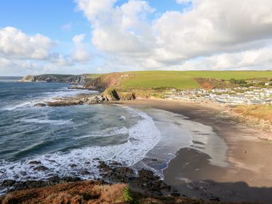 A coastal bay with waves crashing on the shore and houses on the hillside at 2 The Bay in Bigbury