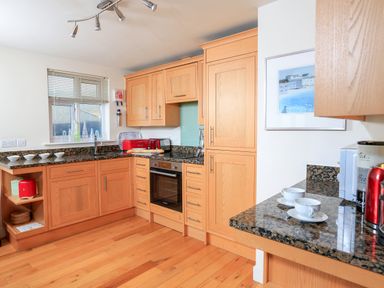 A kitchen with wooden cabinets granite countertops a stove a toaster cups and plates on the counter at 2 The Bay in Bigbury