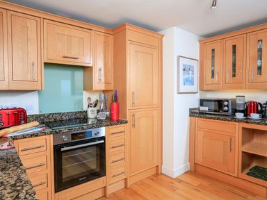 A kitchen with wooden cabinets granite countertops an oven a microwave and kitchen utensils at 2 The Bay in Bigbury