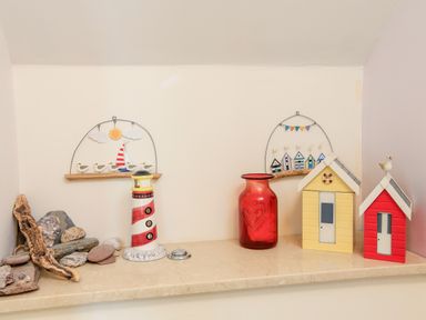 A mantel with decorative beach huts a red vase a lighthouse figurine and stones at 2 The Bay in Bigbury